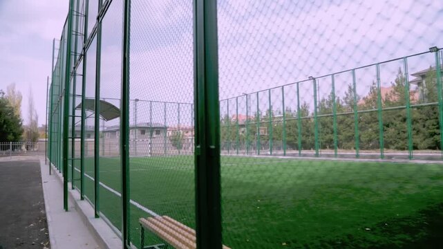 Tashkent, Uzbekistan - 06 06 2025: Empty fenced soccer field with bench on cloudy day