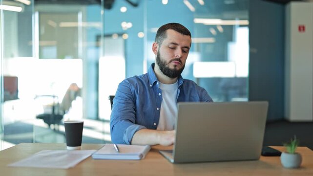 Focused man diligently works on laptop within bright, modern office. Concentrated individual embodies productivity and dedication to business tasks. Creating content, analyzing data, achieving goals.