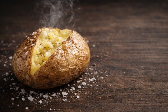 Baked potatoes in their skins on a rustic wooden table. Simple homemade food concept with natural light, warm tones and copy space. Vegetarian comfort food background.