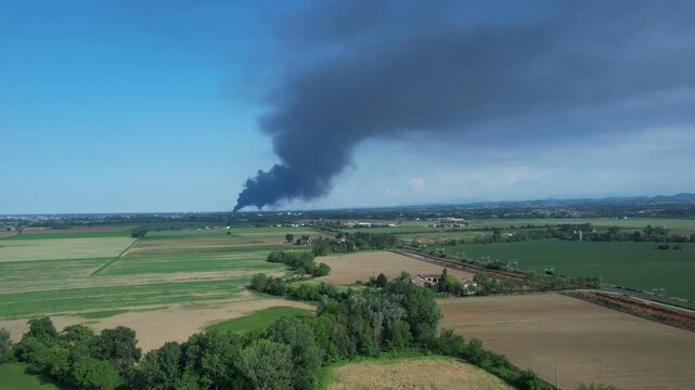 Massive black smoke plume from a plastic manufacturing plant fire moving over rural farmland near Fidenza, northern Italy, revealing air quality hazard, dioxin exposure risk and industrial disaster.