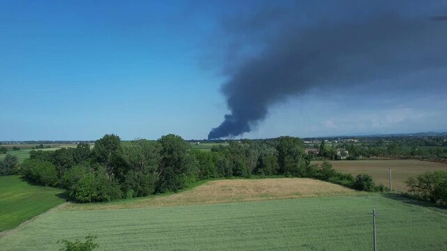 Black smoke from a burning plastic industrial plant spreading over farmland near Via Emilia Fidenza, Emilia Romagna, Italy, showing air pollution, dioxin contamination risk and environmental emergency