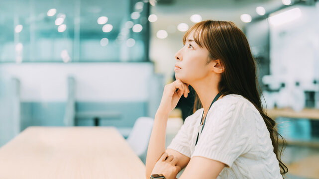 オフィスで頬に手を当てて考える日本人女性,仕事中の思案するビジネスシーン, Japanese woman thinking with her hand on her chin in an office during work