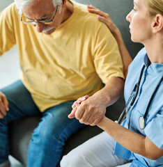 Doctor or nurse caregiver's hand giving support to sad lonely senior man at home or nursing home
