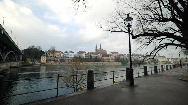 Cinematic pan along the Rhine promenade with Wettsteinbruecke bridge and Basel Minster, Switzerland.