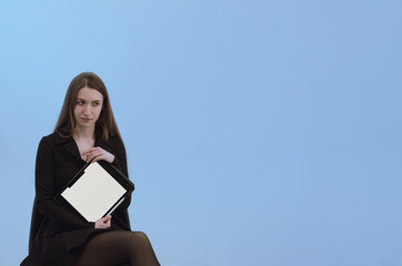Obraz premium Young woman with long hair in black dress show white screen on the tablet. Advertising new app or product. Pale blue background with copy space. Communication concept. Online education, zoom teaching.
