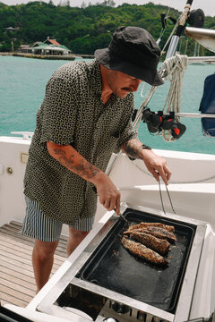 Man Grilling Tuna on Catamaran during Tropical Sailing, Seychell