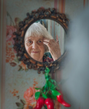 An elderly woman looks at herself in a round mirror