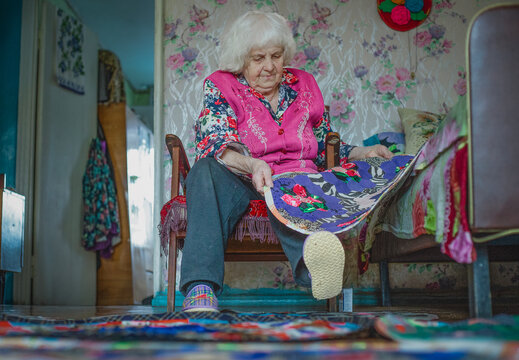 An elderly woman looks at her handicrafts while sitting on a chair