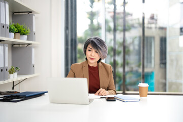 Fototapeta premium Confident mature woman, writer using laptop computer, taking notes, working project in modern office. financier working at workplace. Successful business