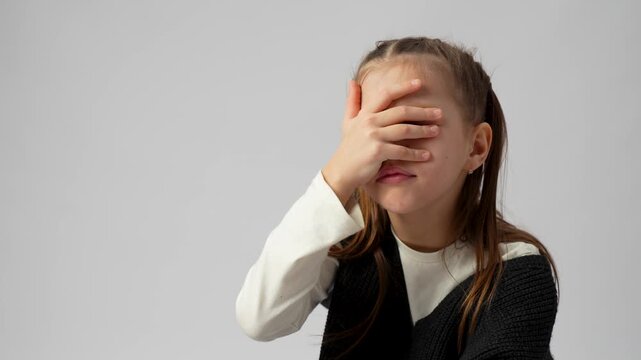 Stressed Young Girl Making Facepalm Gesture.  An expressive young girl covering her eyes with her hand in a facepalm gesture, looking tired or frustrated