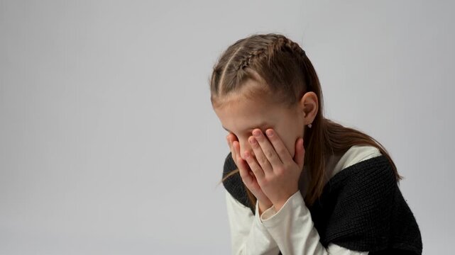 Stressed Young Girl Making Facepalm Gesture.  An expressive young girl covering her eyes with her hand in a facepalm gesture, looking tired or frustrated
