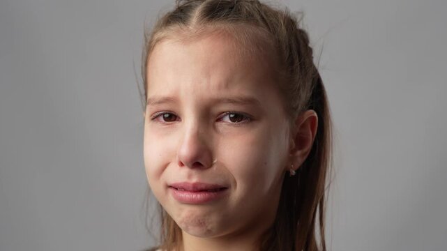 Upset Young Girl Crying and Wiping Tears. A heartrending portrait of a young girl with red, watery eyes wiping away tears with her hand. Studio portrait expressing sadness and grief 