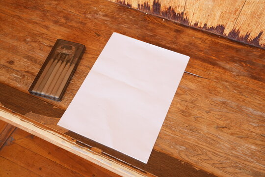 A piece of paper sits on a wooden desk with a pencil case next to it. The pencil case contains six pencils. Concept of creativity and productivity, as the pencils