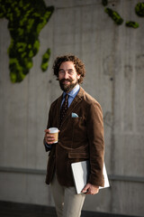 Smiling man holding coffee and laptop near moss map