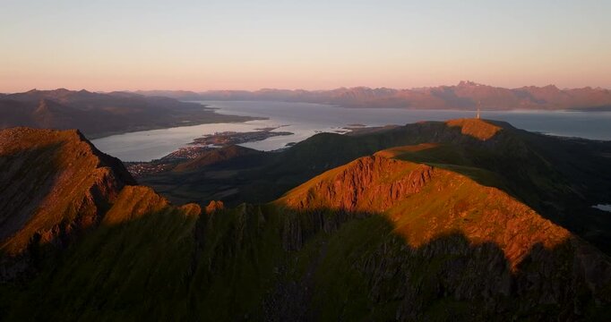 Slow cinematic drone dolly forward above Storheia near Stokmarknes, Hadsel, Norway, revealing fjords, islands and mountain ridges glowing in warm golden hour sunset light