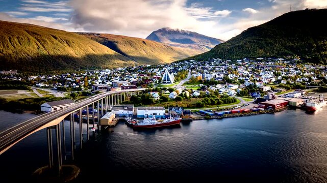 Cinematic drone hyperlapse moving forward above Troms&oslash;, Norway, revealing the city bridge, harbor and fjord landscape with dramatic mountain light and coastal atmosphere