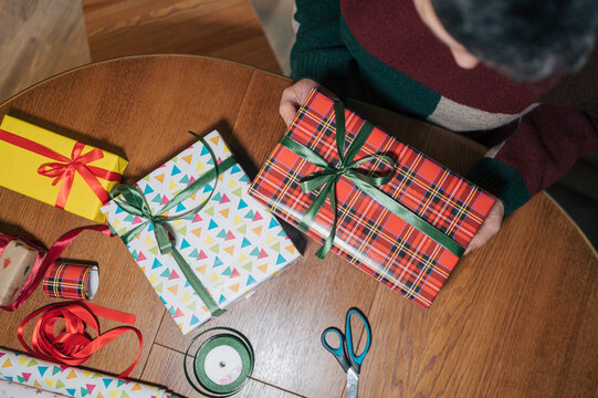 Person wrapping holiday gifts at home with colorful paper and ribbon