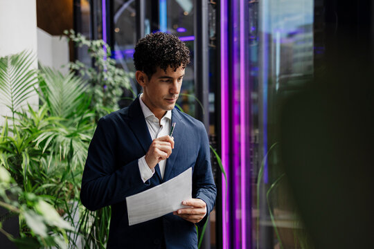 Businessman analyzing document in modern office with plants and technology