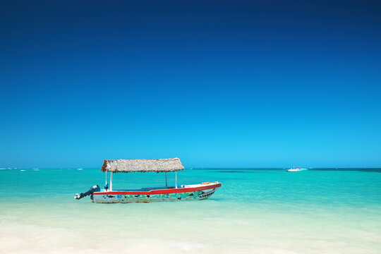 Traditional wooden boat with thatched roof floating on crystal clear turquoise waters of Caribbean sea, near Punta Cana, Dominican republic