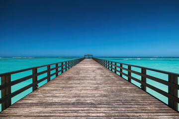 Fototapeta premium Long Wooden Pier in Turquoise Sea against Blue Sky and White Sand Beach, Punta Cana resort, Dominican Republic