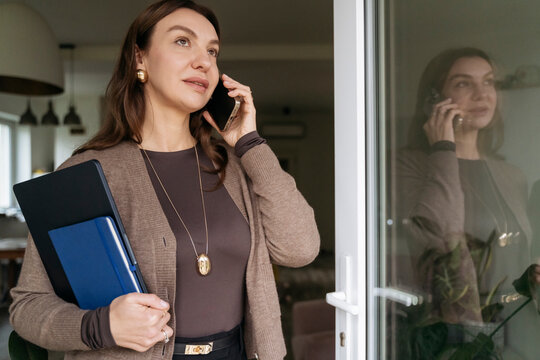 Businesswoman on phone holding folder by window in modern office