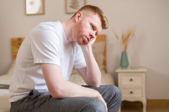 Man sitting on bed appearing sad and stressed in bedroom
