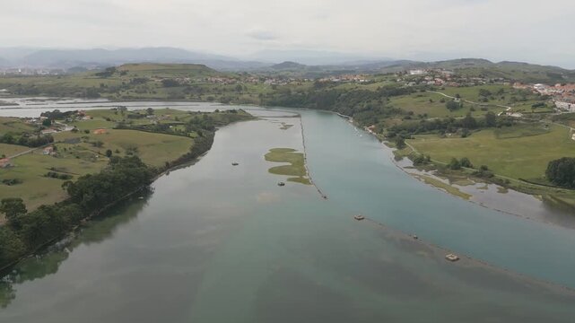A reverse flight over the Suances estuary reveals the river with its deep blue waters, bordered by stone breakwaters. Along the banks, green areas and marshes enhance the estuary's natural beauty.