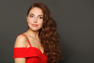 Fototapeta premium Indoor portrait of woman with long hair and make-up on black background. Gorgeous woman with curly hairstyle
