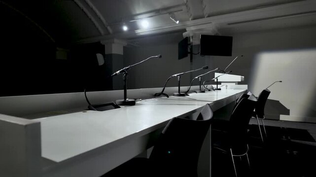 Rows of microphones on a long table in a dimly lit conference room setup