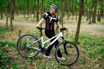 Fototapeta premium Woman cyclist walking with bicycle on sunny path in forest. Taking a break to enjoy scenic views and recover during intense gravel biking session.