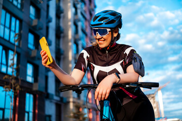 Smiling woman cyclist in sunglasses looking at smartphone screen on city street. Pure pleasure from healthy habits and urban mobility.