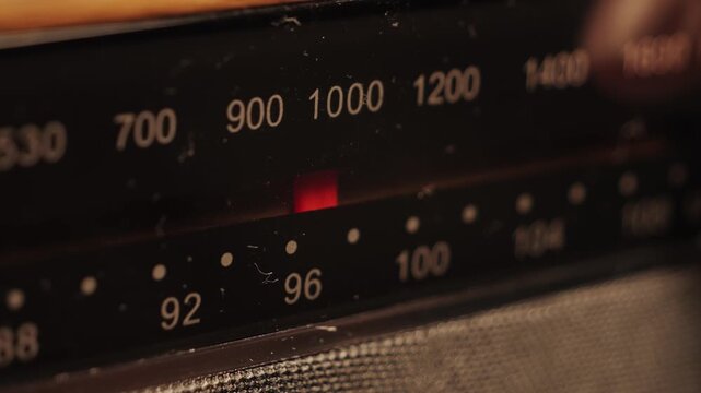 Antique radio tuner red needle sweeps across numbers on reflective face, with station numbers.