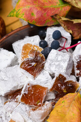 Close-up of powdered turkish delight cubes decorated with wild blue berries and colorful autumn leaves. Traditional oriental seasonal dessert presentation.