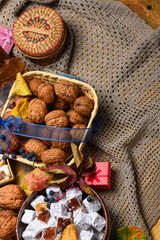 Festive assortment of walnuts in a wicker basket, powdered turkish delight, and autumn leaves on a knitted lace background. Traditional oriental treats with a red gift box for the holidays.