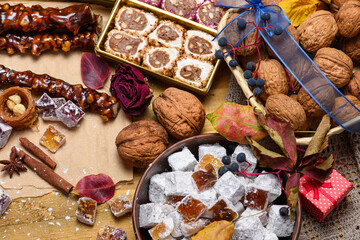 Assorted oriental sweets with kataifi nests, churchkhela, and turkish delight on craft paper. Traditional middle eastern dessert flat lay with walnuts and cinnamon on a wooden background.