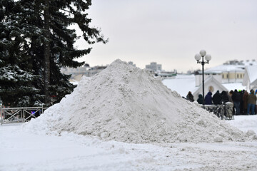Fototapeta premium Massive pile of white snow. Large mound of snow collected by municipal machinery after heavy snowfall in city square to clear roads and sidewalks for safe urban transportation and pedestrian access