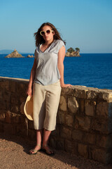 Young woman leaning on a stone wall at the seaside resort, enjoying the warm light and beauty of the summer sunset.