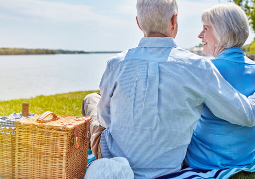 Picnic, old couple and embrace at lake for love, support and relax together on blanket on vacation. Hug, senior man and woman outdoor on holiday with back view, smile and connection in retirement