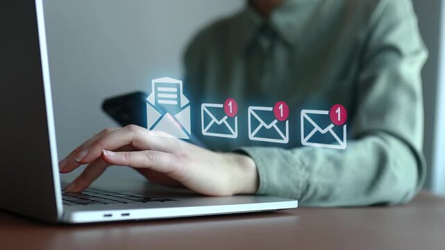 Person checks email on laptop while holding phone with notifications on screen in a simple workspace setting.