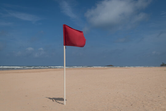 Red flag on pole warning on serene beach near ocean with waves and copy space