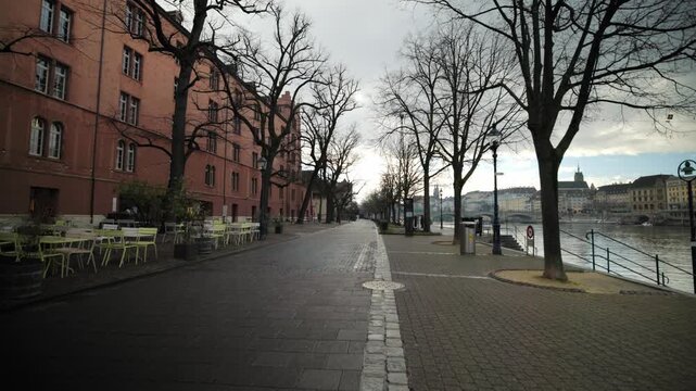 Scenic riverside promenade with pan and with bare trees and historical buildings along the Rhine in Basel, Switzerland.