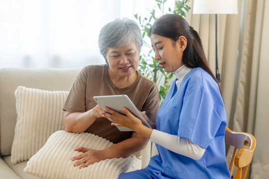 Caregiver explains guidance using a digital tablet during a senior support visit, caregiving, healthcare communication at home. Caregiver Reviewing Notes on Tablet With Elderly Patient.