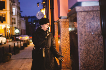 Obraz premium Surprised Woman in Black Beret Looking at Shop Window on Night City Street