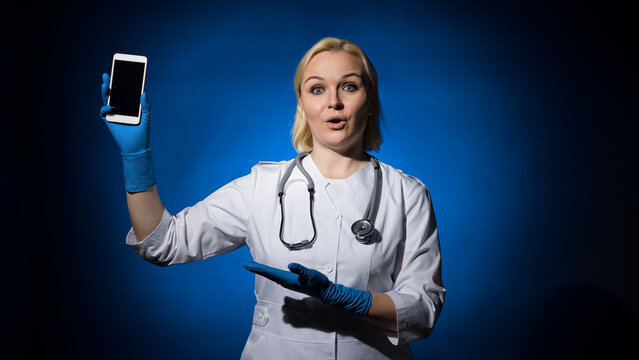 female doctor points to the phone in her hand. blue and dark background
