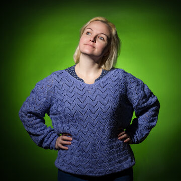 an adult woman in a blue knitted sweater stands with her hands at her sides and looks to the side