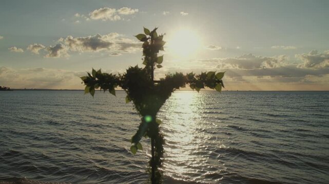 Cross covered in lush leaves sways in ocean breeze at sunset, ocean waves glisten behind in calm serene static shot by Generative AI