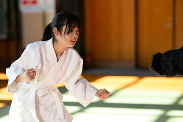 道場で鋭い眼差しで後ろを振り返り蹴りを放つ空手着の女の子　護身術と防犯のイメージ