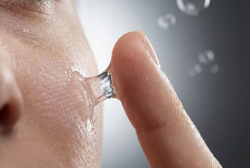 Fototapeta premium Close-up of a person peeling transparent facial gel mask from smooth skin. Skincare concept with hydration and beauty treatment. Soft lighting highlights texture and freshness of healthy skin.