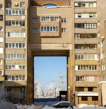 A winter city courtyard with gray multi-story panel buildings (Khrushchev-era or Brezhnev-era buildings) covered in a thin layer of snow and frost, under a bright blue sky