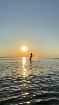 Young woman walking on stand up paddle sup boards by the sea during summer vacation. Beautiful girl flat water paddling against sea and sky background. Slow motion